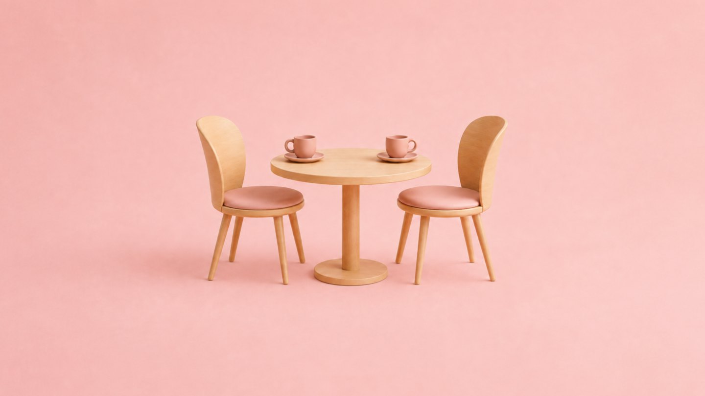 Une petite table ronde en bois clair, deux chaises face à face et deux tasses de café, sur fond rose.
